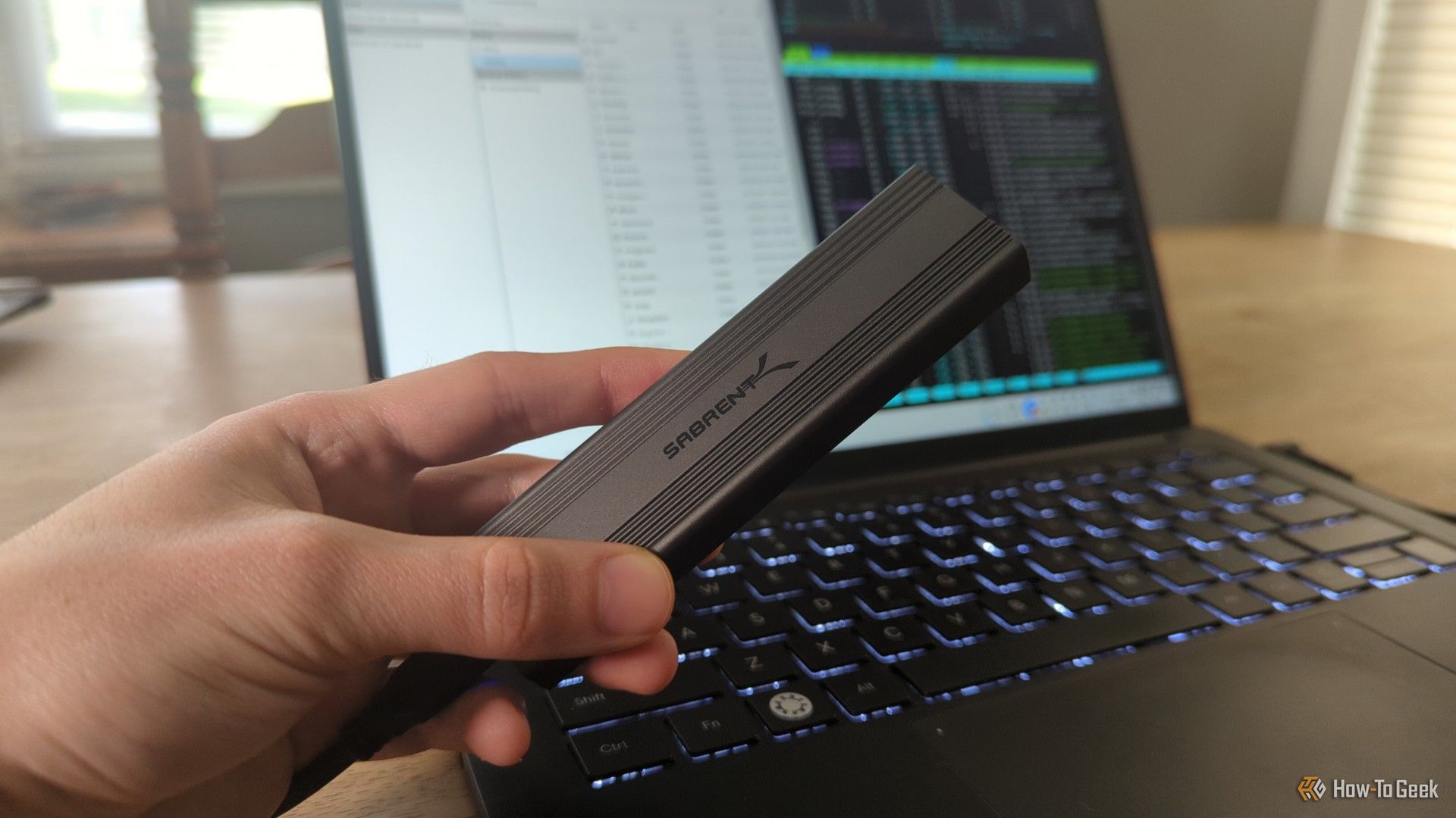 a-person-s-hand-holding-a-sabrent-external-ssd-drive-in-front-of-a-linux-laptop.jpg